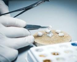 Two dental crowns on dark reflective surface
		  Lab technician’s gloved hands working on crowns
		  