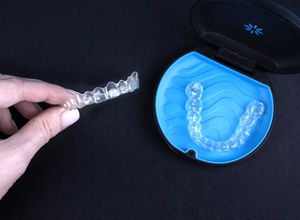 Two Invisalign aligners, one in case and one in hand