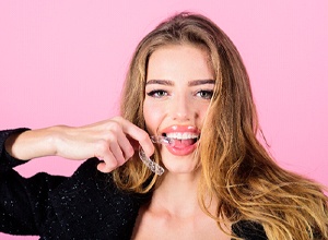 Smiling young woman holding clear aligner close to mouth