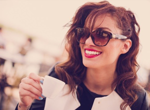 Woman in sunglasses holding white coffee cup outdoors