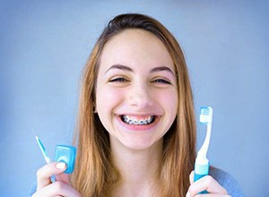 Smiling girl with braces holding floss and toothbrush