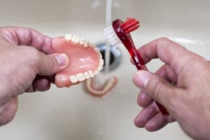 Close-up of man’s hands carefully cleaning dentures over sink