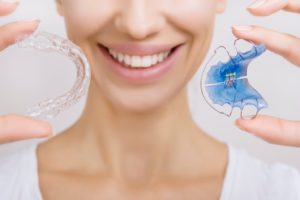 Smiling woman holding two Invisalign retainers in Enfield