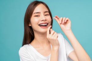 Smiling young woman with braces, flossing her teeth