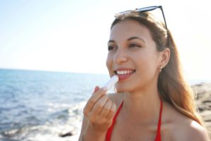 Woman on beach, applying SPF lip balm