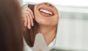 Woman’s beautiful smile reflected in tooth-shaped mirror